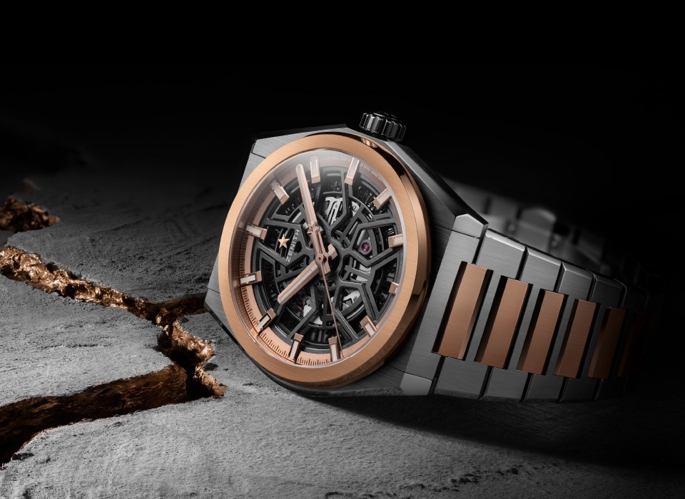 Skeleton-dial wristwatch with rose gold bezel and two-tone metal bracelet, resting on a rock with a copper vein, dark moody background